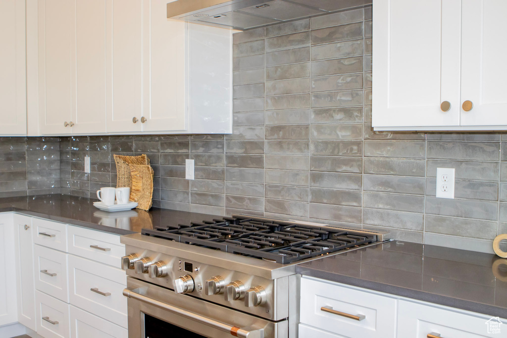 Kitchen with white cabinetry, high end stove, backsplash, and wall chimney exhaust hood