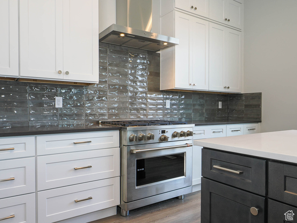 Kitchen with white cabinetry, hardwood / wood-style flooring, backsplash, wall chimney range hood, and designer stove