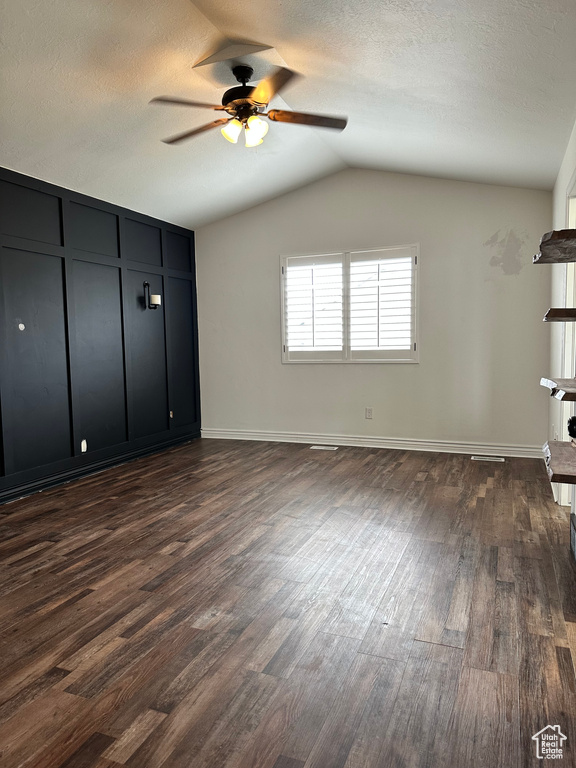 Unfurnished bedroom featuring dark hardwood / wood-style floors, a textured ceiling, vaulted ceiling, and ceiling fan