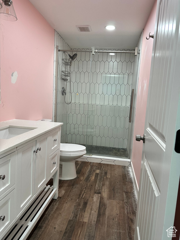 Bathroom featuring wood-type flooring, toilet, vanity, and tiled shower