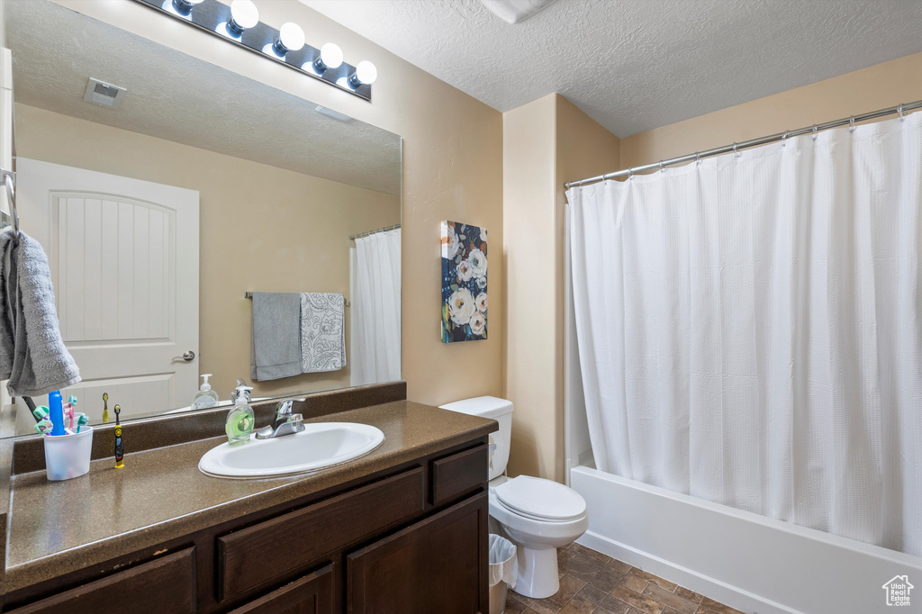Full bathroom featuring vanity, toilet, a textured ceiling, and shower / bath combo with shower curtain