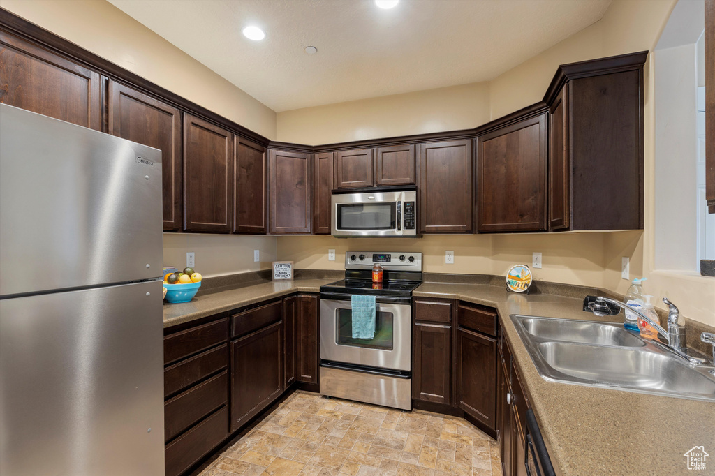 Kitchen featuring appliances with stainless steel finishes, light tile floors, sink, and dark brown cabinets