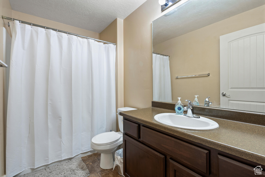 Bathroom featuring toilet, vanity with extensive cabinet space, tile flooring, and a textured ceiling
