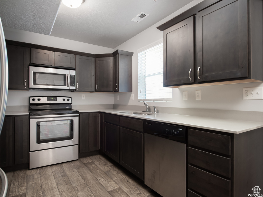 Kitchen with appliances with stainless steel finishes, dark brown cabinets, sink, and light hardwood / wood-style floors