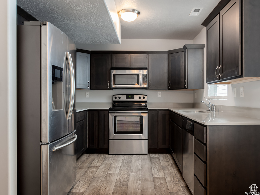 Kitchen featuring appliances with stainless steel finishes, light wood-type flooring, sink, and dark brown cabinets