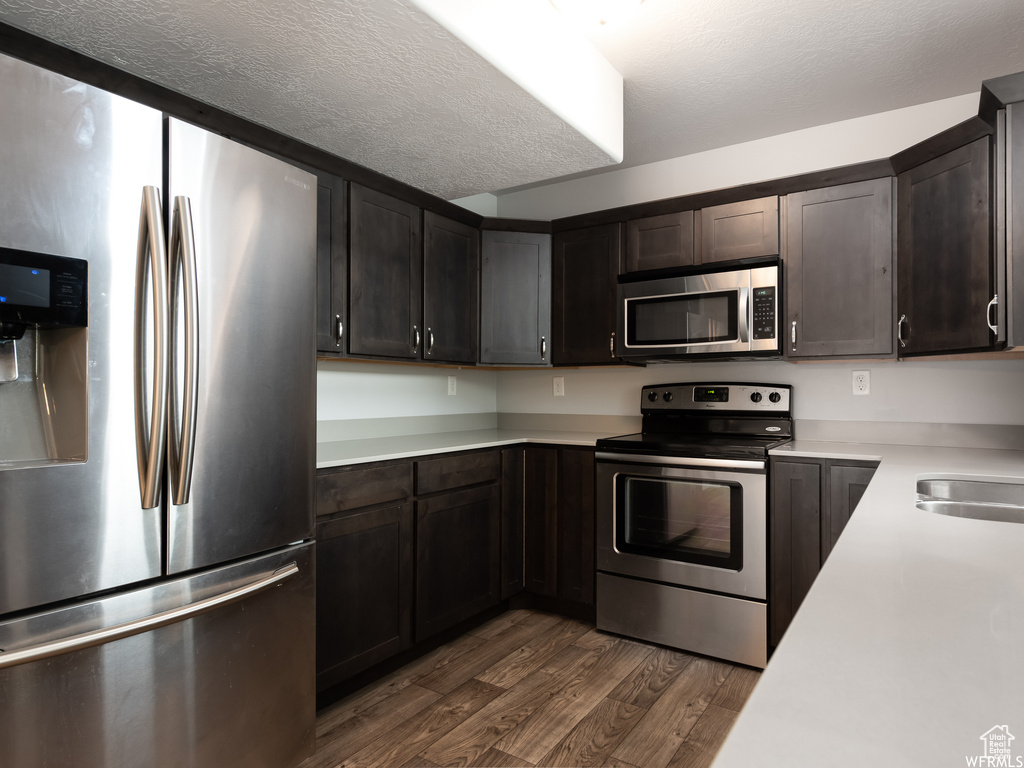 Kitchen with dark hardwood / wood-style floors, appliances with stainless steel finishes, sink, and dark brown cabinets