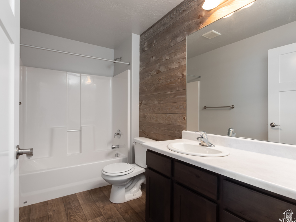 Full bathroom with hardwood / wood-style flooring, wooden walls, vanity, washtub / shower combination, and toilet