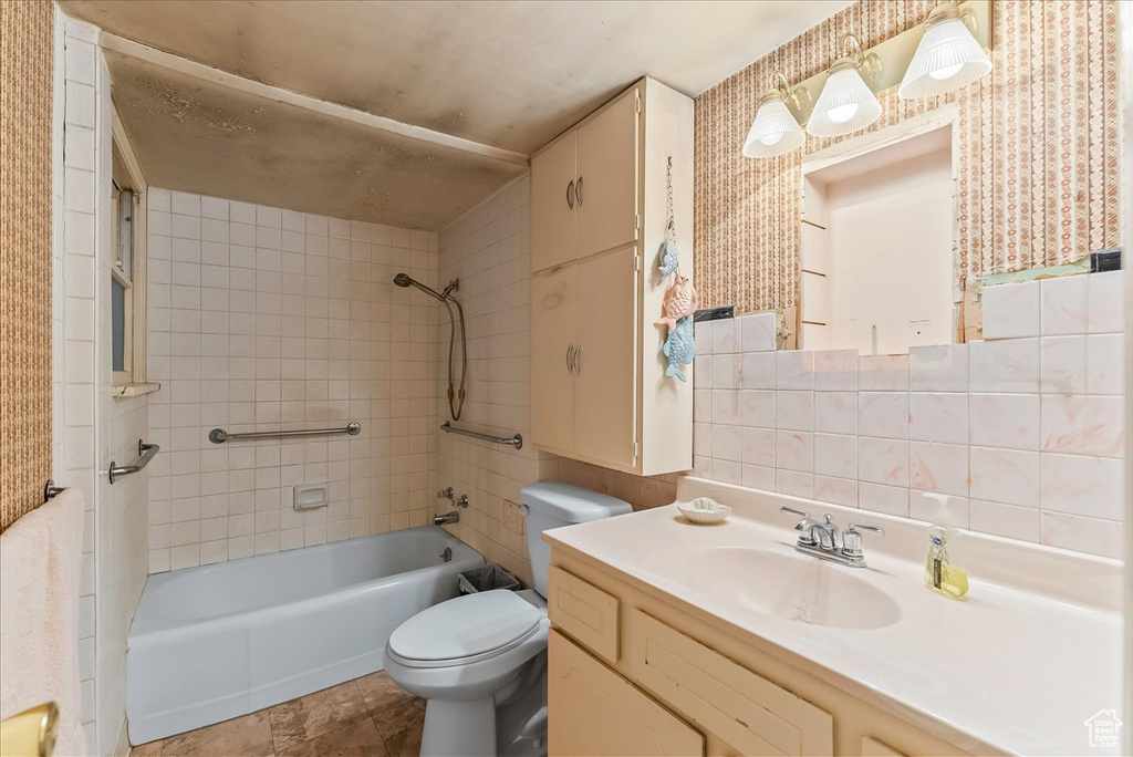Full bathroom with tile walls, tile flooring, oversized vanity, toilet, and tiled shower / bath combo