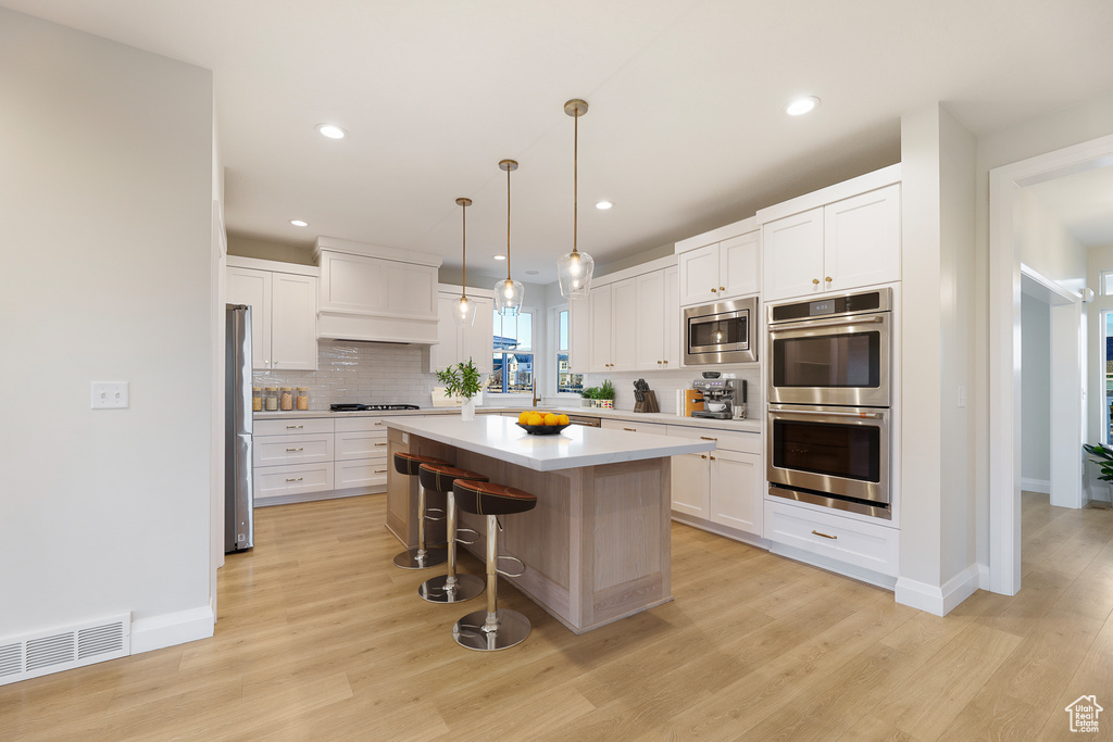 Kitchen with a kitchen island, light hardwood / wood-style flooring, white cabinetry, and stainless steel appliances
