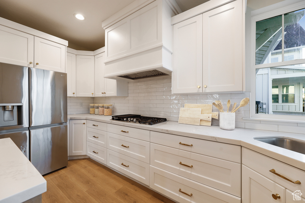 Kitchen with white cabinetry, tasteful backsplash, appliances with stainless steel finishes, light wood-type flooring, and light stone counters
