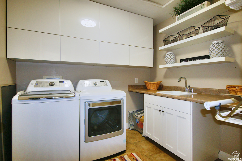 Clothes washing area featuring sink, washer and clothes dryer, light tile floors, and cabinets