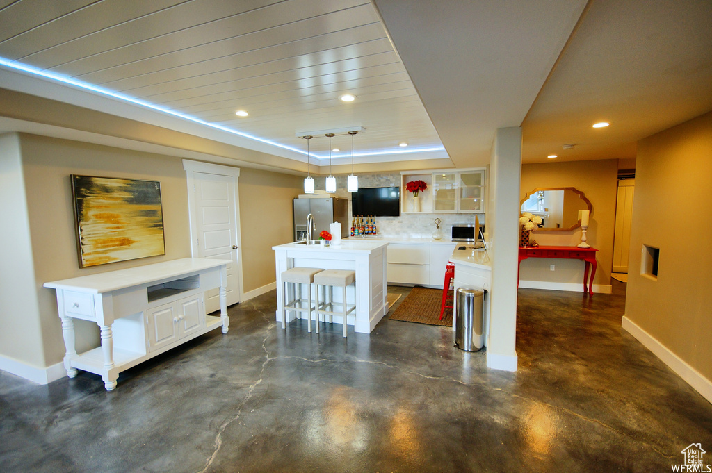 Interior space with tasteful backsplash, a kitchen breakfast bar, white cabinetry, pendant lighting, and an island with sink
