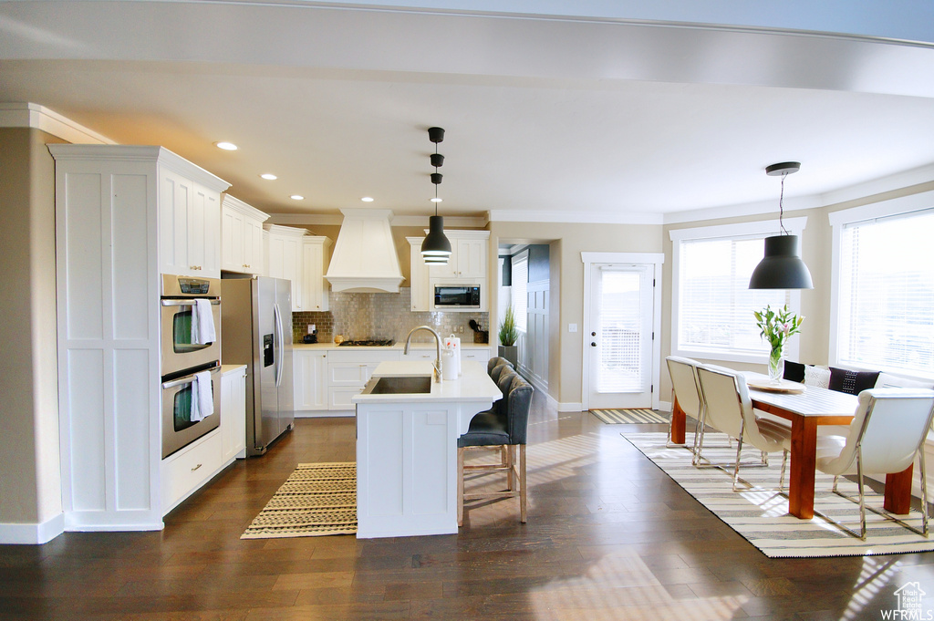 Kitchen with custom exhaust hood, dark hardwood / wood-style flooring, stainless steel appliances, and hanging light fixtures
