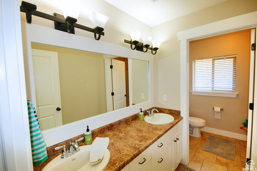 Bathroom featuring tile flooring, vanity with extensive cabinet space, dual sinks, and toilet