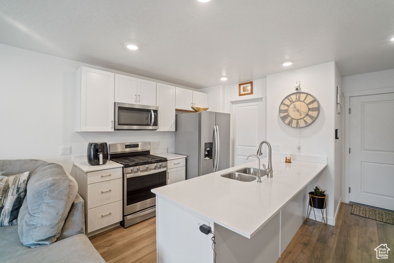 Kitchen with appliances with stainless steel finishes, a breakfast bar area, sink, white cabinetry, and light hardwood / wood-style flooring