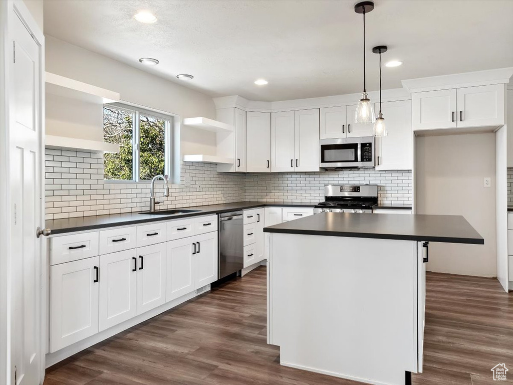 Kitchen with stainless steel appliances, pendant lighting, sink, a kitchen island, and dark wood-type flooring