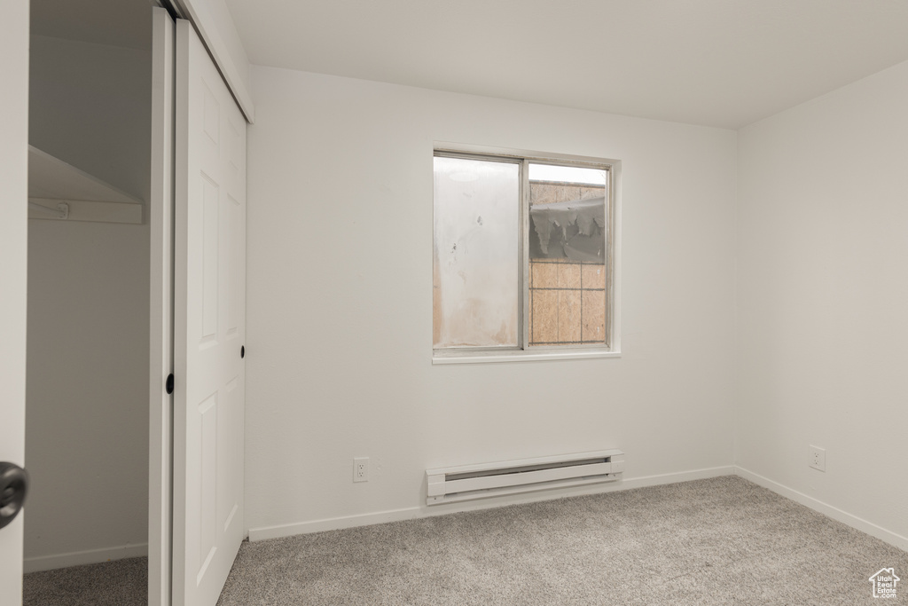 Unfurnished bedroom with a baseboard radiator, light colored carpet, and a closet