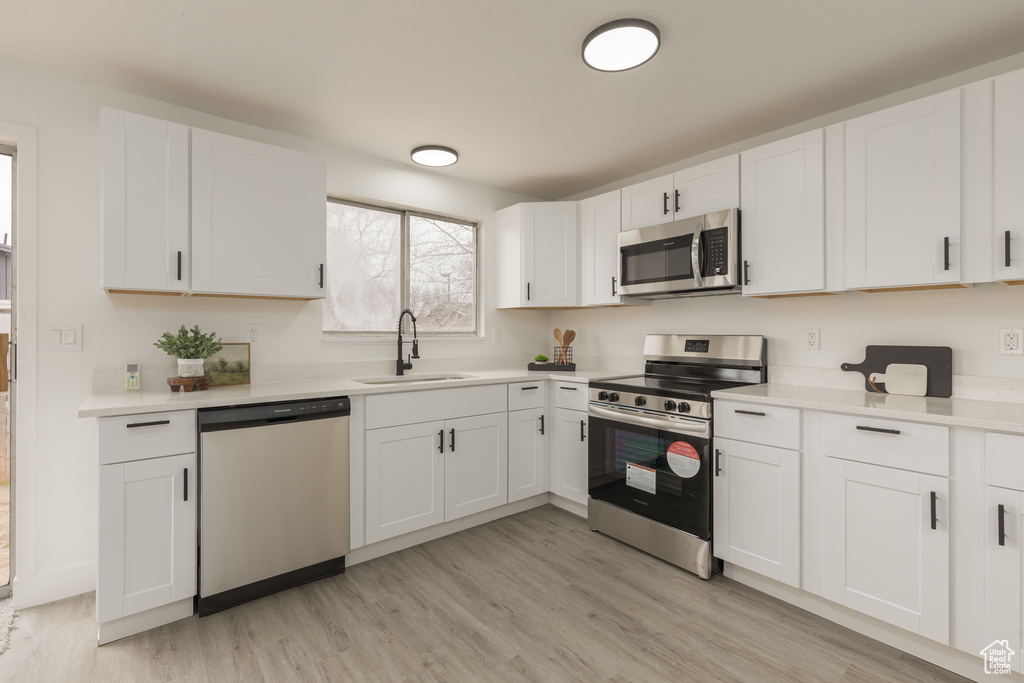 Kitchen featuring sink, white cabinets, stainless steel appliances, and light hardwood / wood-style floors