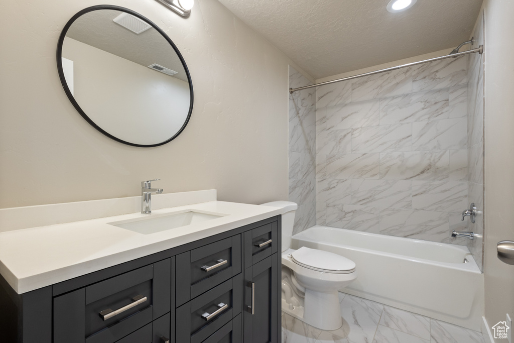 Full bathroom with vanity, a textured ceiling, tiled shower / bath, toilet, and tile flooring