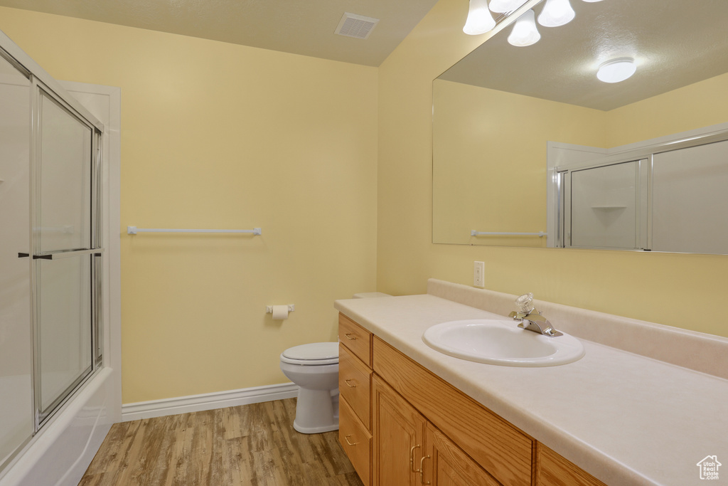 Full bathroom featuring shower / bath combination with glass door, toilet, large vanity, and hardwood / wood-style floors