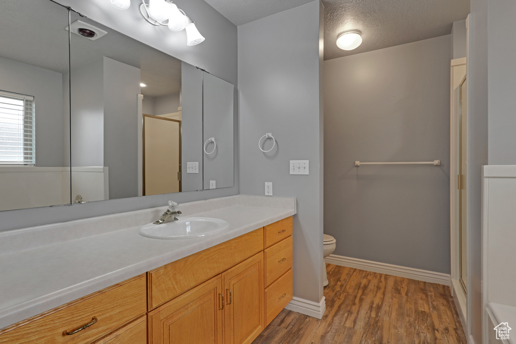 Bathroom featuring hardwood / wood-style floors, a textured ceiling, toilet, an enclosed shower, and vanity