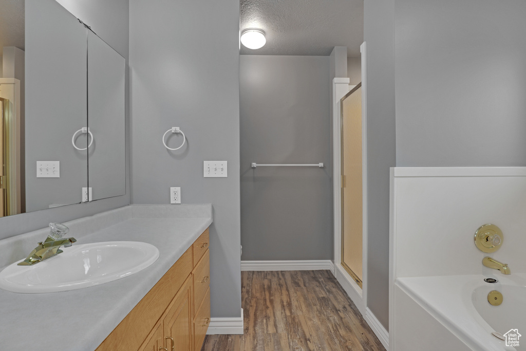 Bathroom with a textured ceiling, separate shower and tub, large vanity, and hardwood / wood-style floors