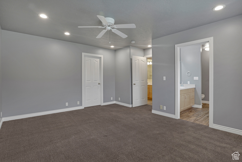 Unfurnished bedroom with ensuite bathroom, ceiling fan, a closet, and dark carpet