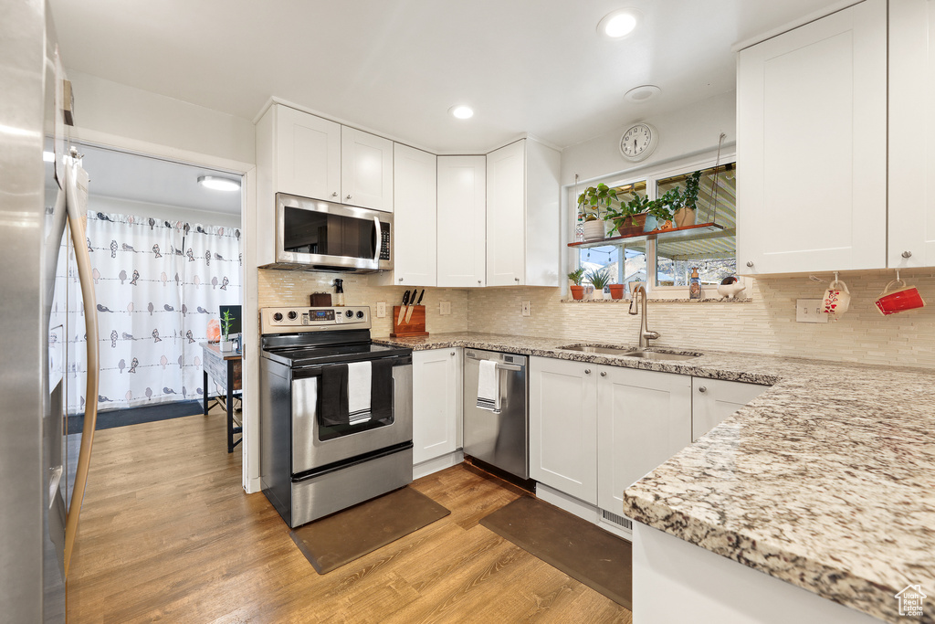Kitchen featuring white cabinetry, sink, tasteful backsplash, light wood-type flooring, and stainless steel appliances