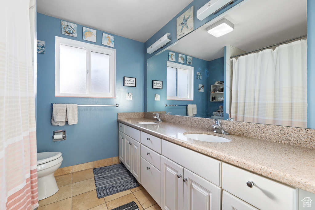 Bathroom featuring tile floors, large vanity, dual sinks, and toilet
