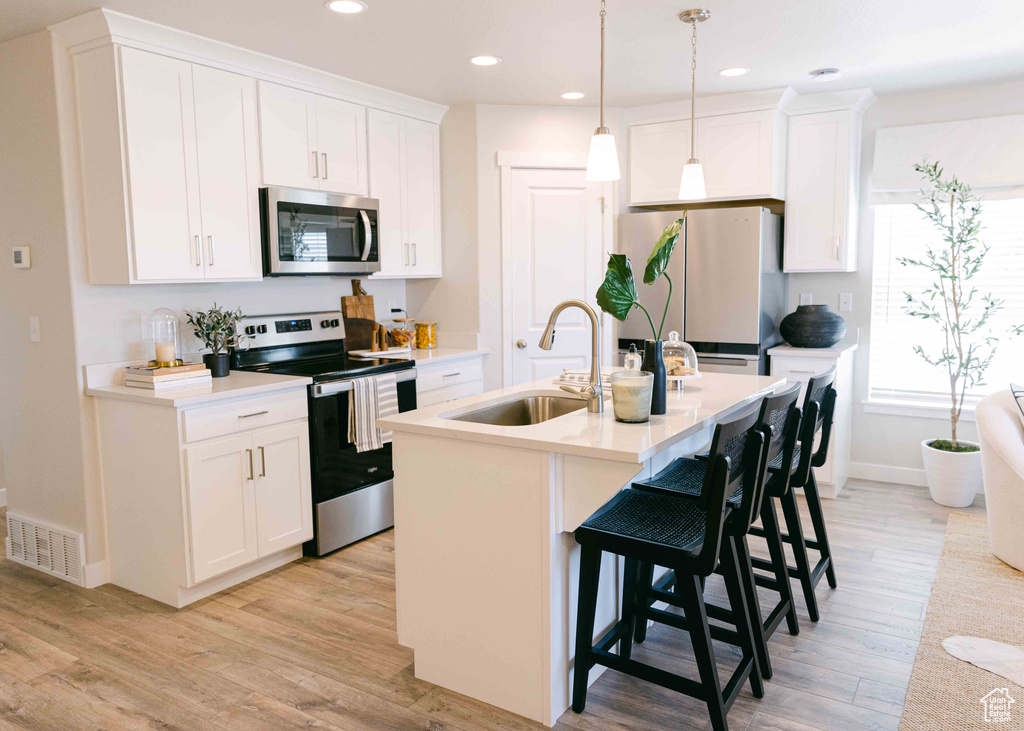 Kitchen with stainless steel appliances, light hardwood / wood-style floors, sink, hanging light fixtures, and an island with sink