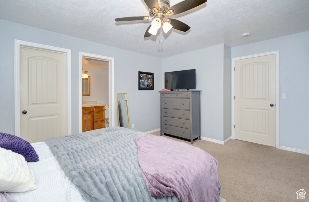 Carpeted bedroom with a textured ceiling, connected bathroom, and ceiling fan