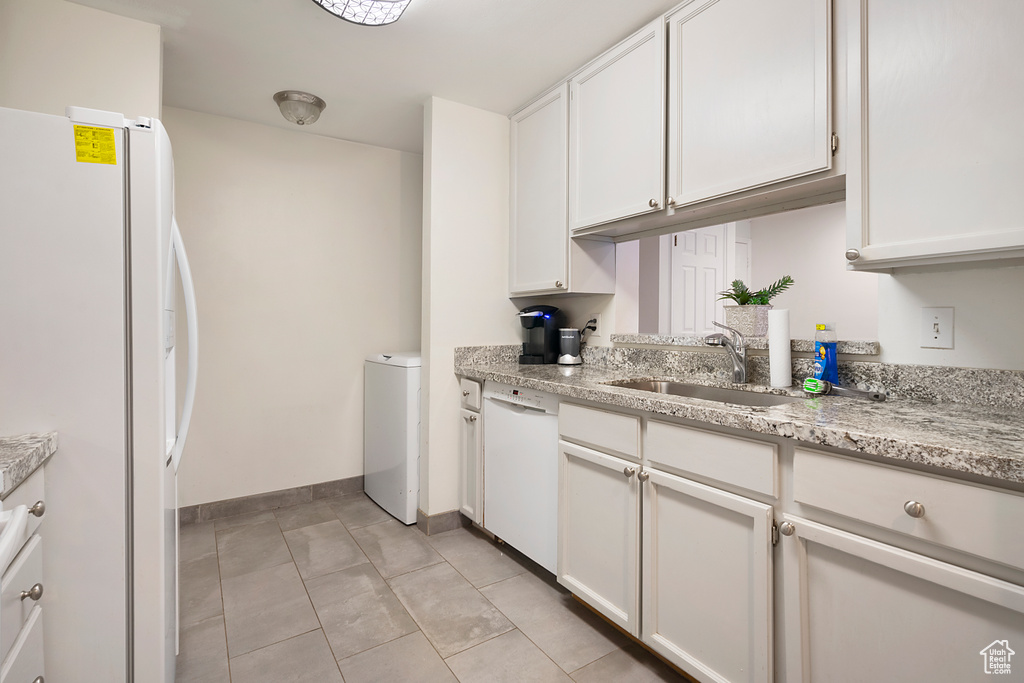 Kitchen featuring sink, white cabinets, white appliances, light tile floors, and light stone counters