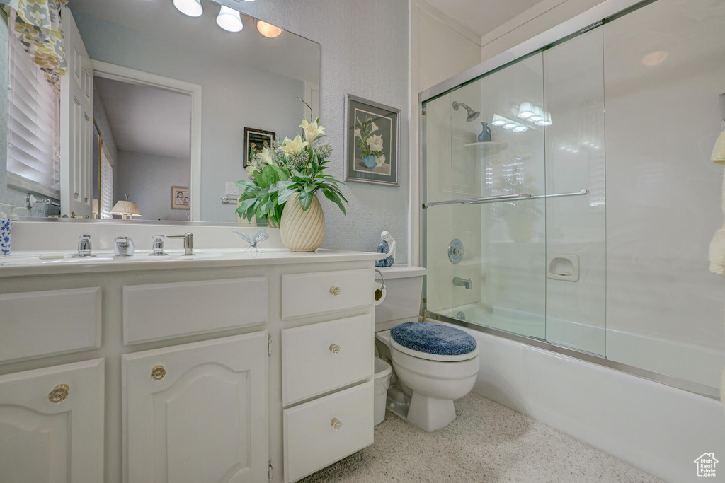 Full bathroom with bath / shower combo with glass door, toilet, and vanity