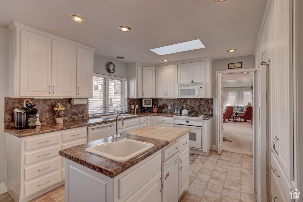 Kitchen featuring white cabinetry, a skylight, white appliances, light colored carpet, and an island with sink