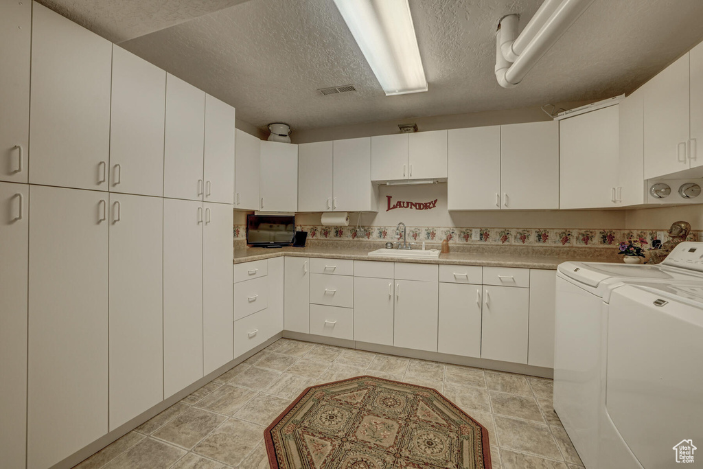 Kitchen with sink, white cabinets, washing machine and dryer, and light tile floors