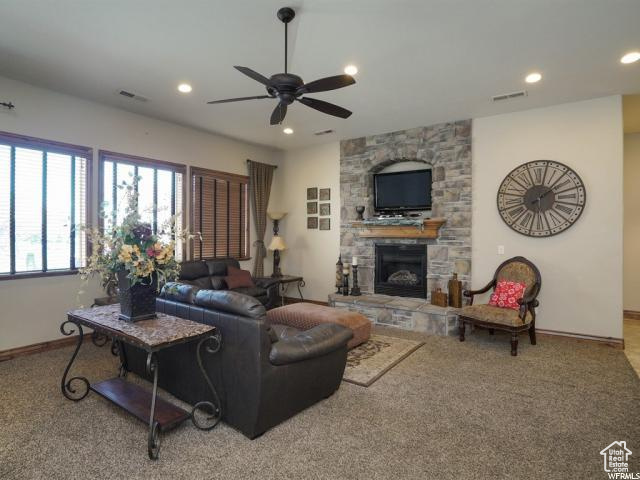 Living room featuring ceiling fan, light colored carpet, and a stone fireplace