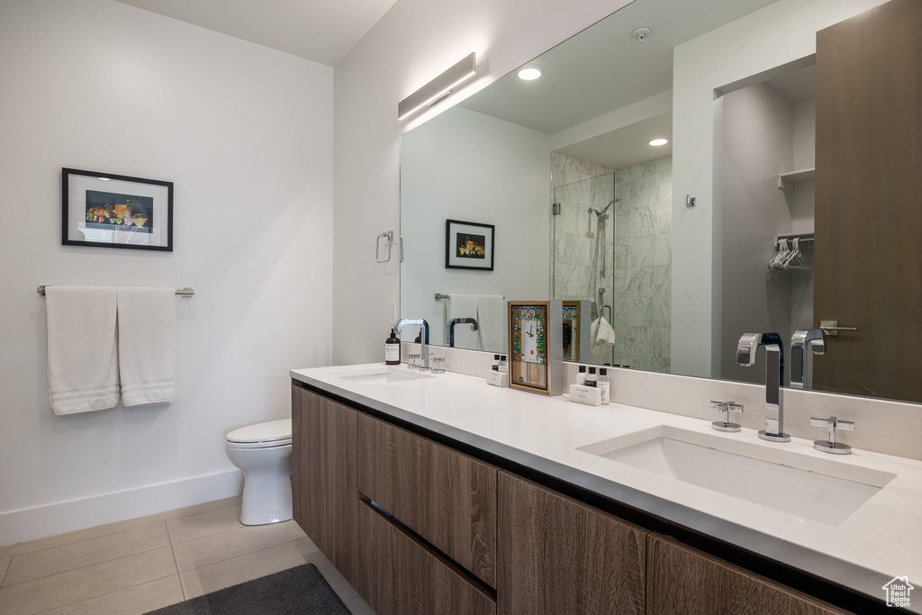 Bathroom featuring dual vanity, toilet, a shower with door, and tile flooring