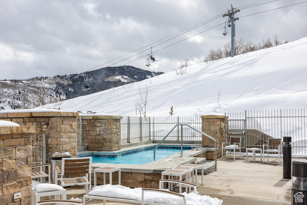 Snow covered pool featuring a mountain view and a patio