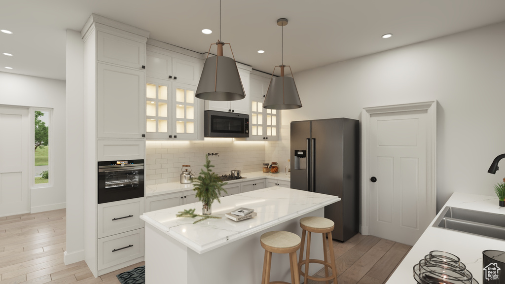 Kitchen featuring white cabinets, tasteful backsplash, black appliances, a kitchen island, and light wood-type flooring