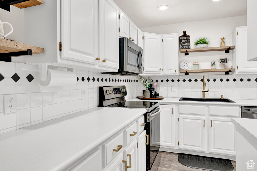 Kitchen with white cabinetry, stainless steel appliances, sink, and backsplash