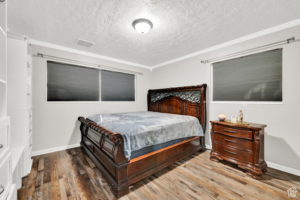 Bedroom featuring hardwood / wood-style flooring, a textured ceiling, and crown molding