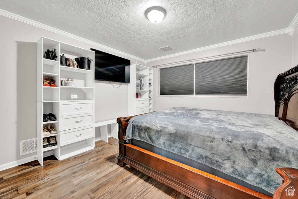 Bedroom with a textured ceiling, ornamental molding, and light hardwood / wood-style floors