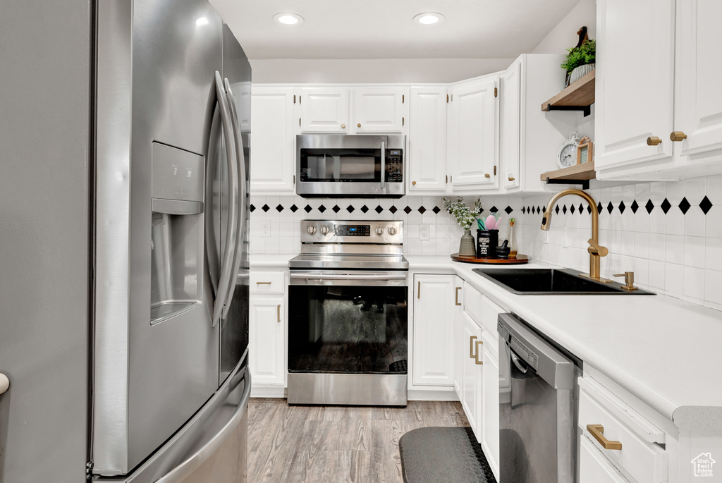 Kitchen featuring tasteful backsplash, white cabinets, stainless steel appliances, light hardwood / wood-style floors, and sink
