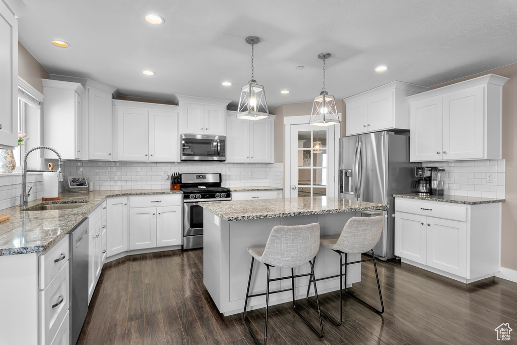 Kitchen featuring tasteful backsplash, stainless steel appliances, dark wood-type flooring, a center island, and light stone countertops