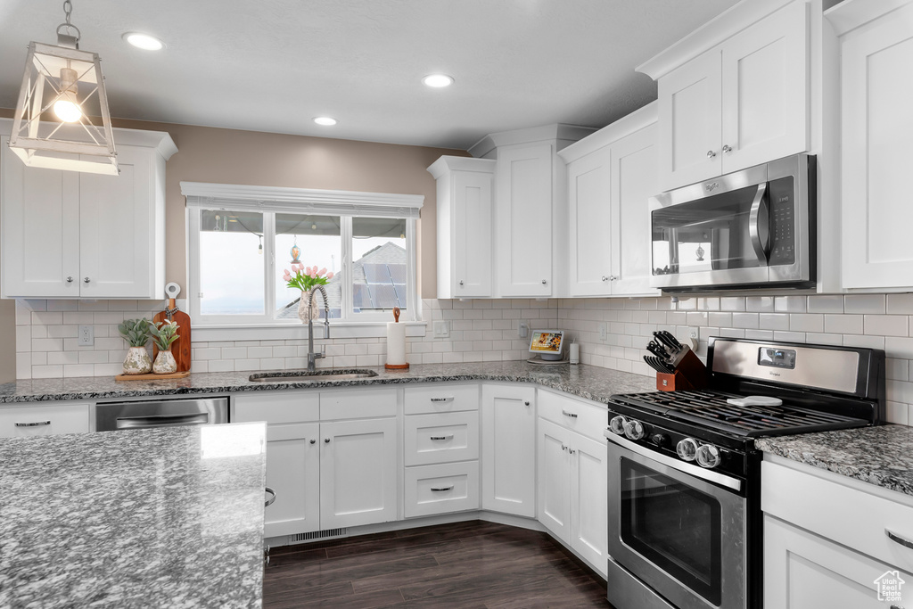 Kitchen featuring white cabinetry, sink, pendant lighting, backsplash, and stainless steel appliances