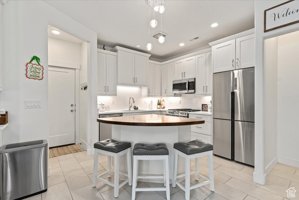 Kitchen featuring appliances with stainless steel finishes, light tile floors, white cabinetry, and a center island