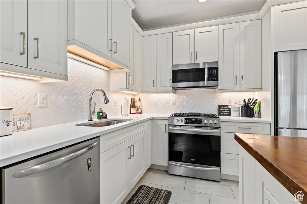 Kitchen featuring backsplash, light tile floors, stainless steel appliances, sink, and white cabinetry