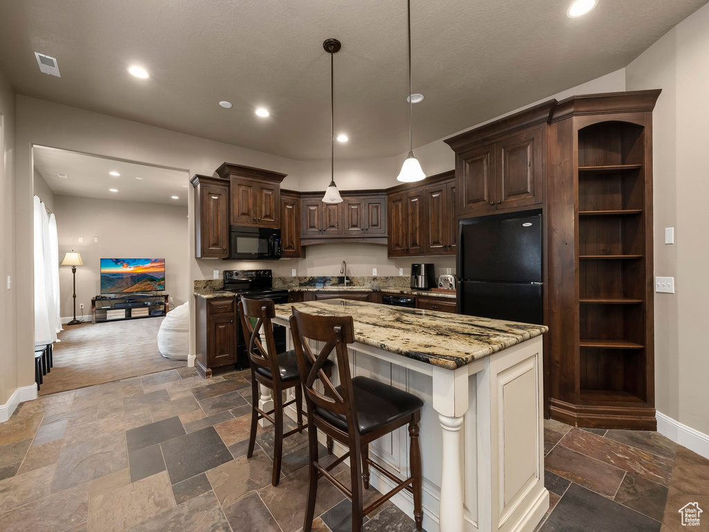Kitchen with dark tile flooring, a kitchen bar, black appliances, a kitchen island, and light stone counters