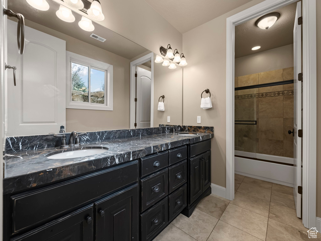 Bathroom featuring dual sinks, tile flooring, bath / shower combo with glass door, and oversized vanity