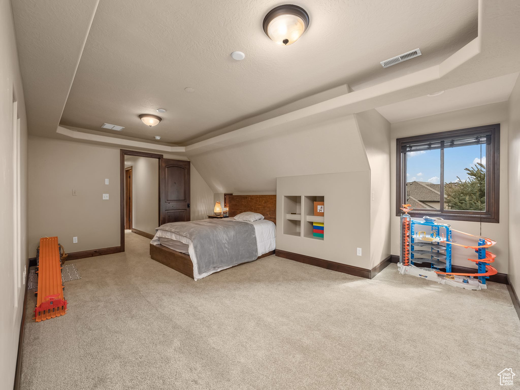 Bedroom featuring a raised ceiling, light carpet, a textured ceiling, and lofted ceiling